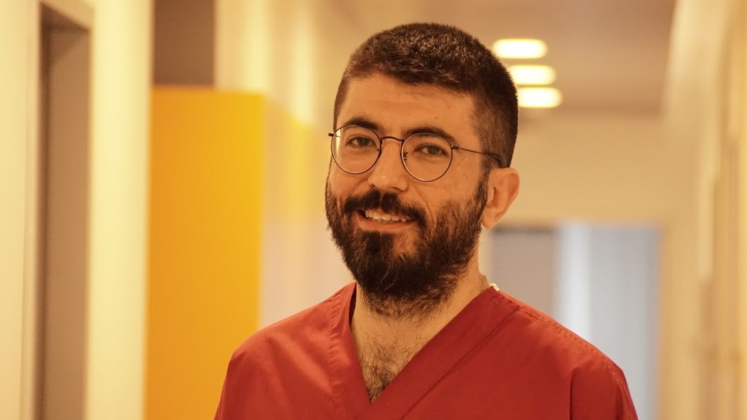 Diş eti doktoru (Periodontolog)  Çağdaş Çağlar Laçin. Operasyon kıyafeti giymiş. Gülümsüyor.