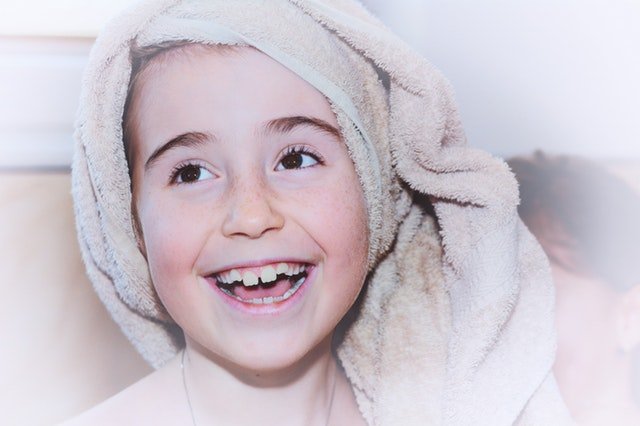 Banyo sonrası havlulara sarılmış bir kız 7 yaşında. Eksik dişlerine rağmen gülümsüyor.
